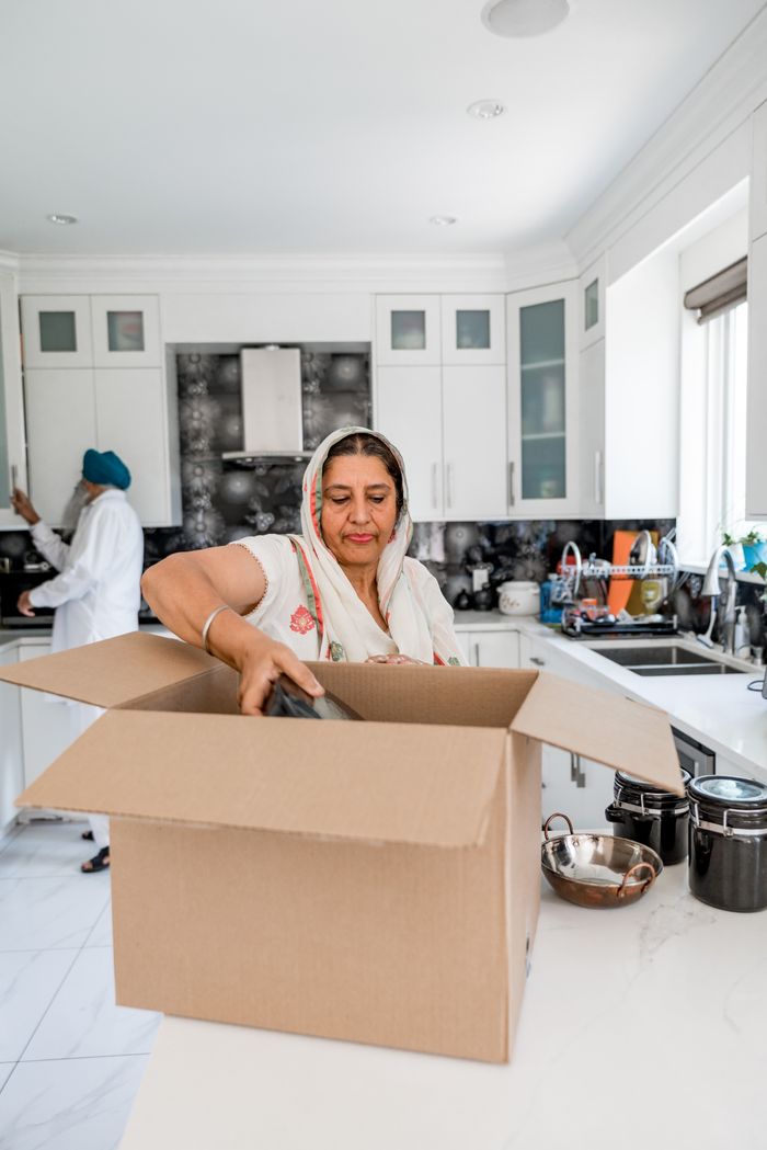A woman unpacks cardboard boxes in a bright, modern kitchen setting.