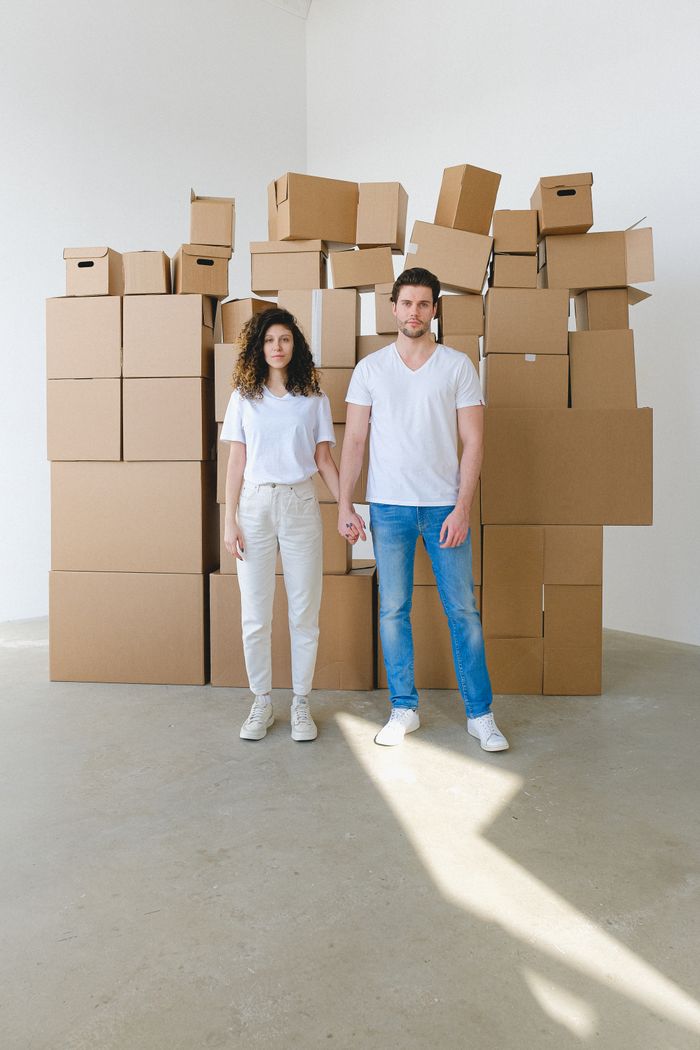 Couple standing and holding hands in front of a pile of cardboard boxes indoors.
